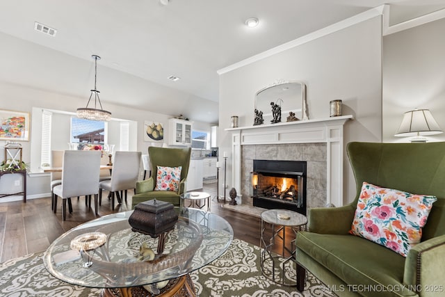 living room with a tiled fireplace, dark wood-type flooring, ornamental molding, and vaulted ceiling