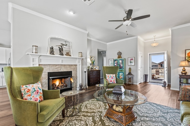 living room featuring crown molding, ceiling fan, dark hardwood / wood-style flooring, and a tiled fireplace