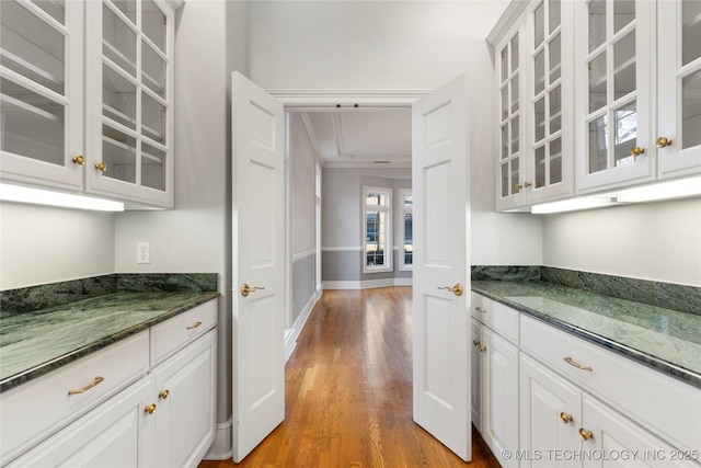 bar with white cabinets, light wood-type flooring, and dark stone counters