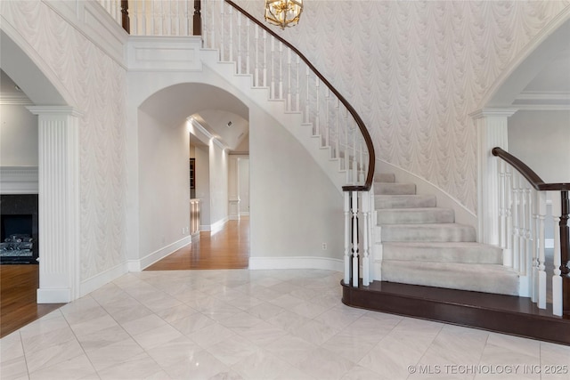 stairs featuring crown molding, a towering ceiling, and decorative columns