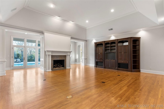 unfurnished living room featuring crown molding, light wood-type flooring, a high end fireplace, and a towering ceiling