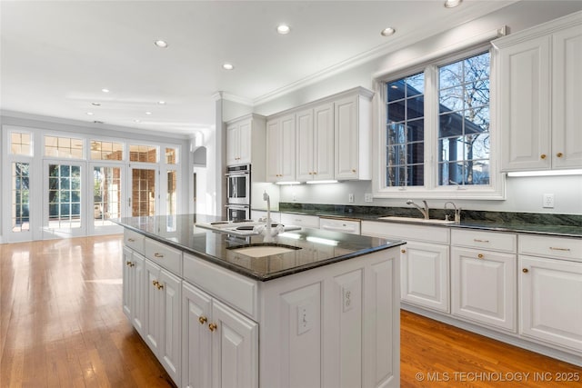 kitchen featuring a kitchen island with sink, sink, and white cabinetry