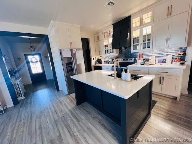 kitchen with a center island with sink, custom exhaust hood, white cabinets, and appliances with stainless steel finishes