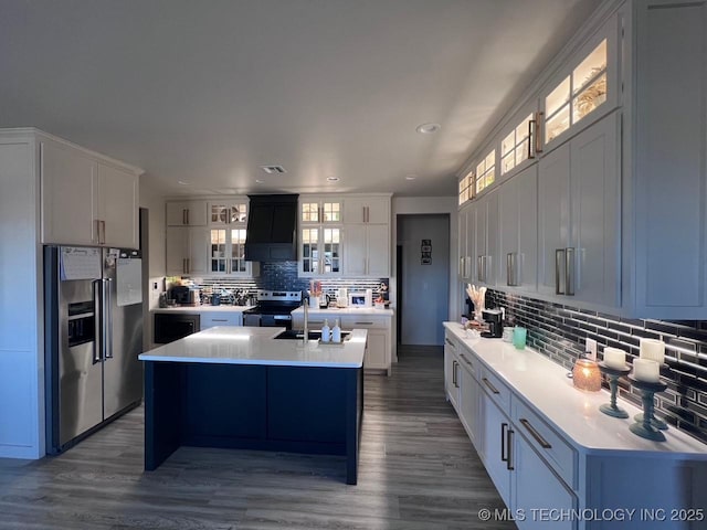 kitchen with sink, white cabinetry, backsplash, stainless steel appliances, and an island with sink