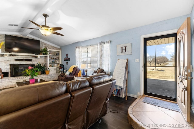 living room featuring vaulted ceiling with beams, dark wood-type flooring, a brick fireplace, and ceiling fan