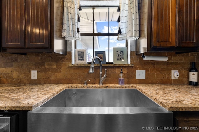 kitchen with dark brown cabinetry, sink, decorative backsplash, and light stone countertops