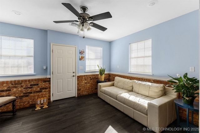 living room featuring plenty of natural light, dark hardwood / wood-style floors, ceiling fan, and brick wall