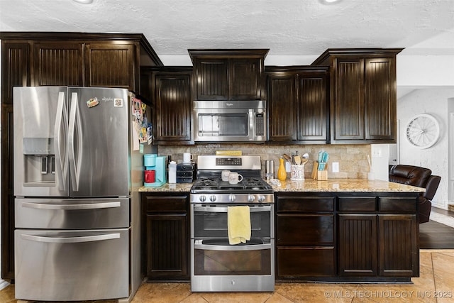 kitchen featuring light stone counters, dark brown cabinets, stainless steel appliances, and decorative backsplash