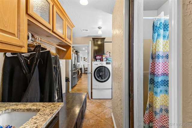 washroom with washer / clothes dryer, a textured ceiling, and light tile patterned floors