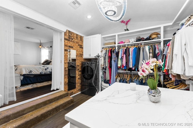 spacious closet with separate washer and dryer, dark wood-type flooring, vaulted ceiling, and a chandelier