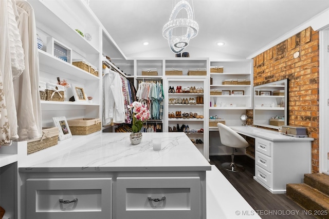 spacious closet with vaulted ceiling, dark hardwood / wood-style floors, built in desk, and a notable chandelier