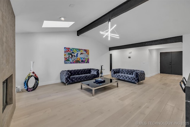 living room with a large fireplace, vaulted ceiling with skylight, and light hardwood / wood-style flooring