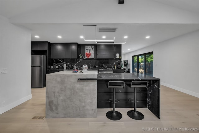 kitchen with stainless steel refrigerator, tasteful backsplash, a breakfast bar area, and light hardwood / wood-style flooring