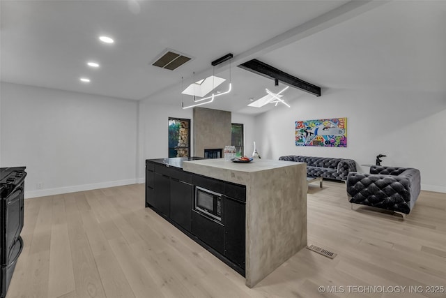 kitchen with pendant lighting, light wood-type flooring, vaulted ceiling with skylight, and a kitchen island