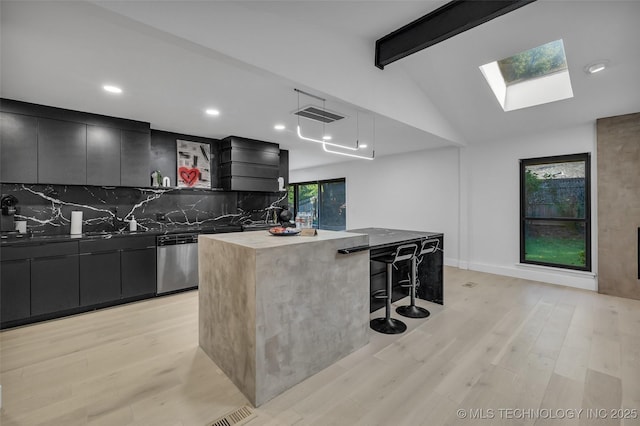 kitchen featuring lofted ceiling with skylight, a breakfast bar, pendant lighting, dishwasher, and decorative backsplash