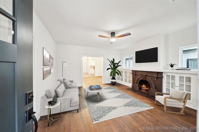 living room with wood-type flooring, a brick fireplace, and ceiling fan