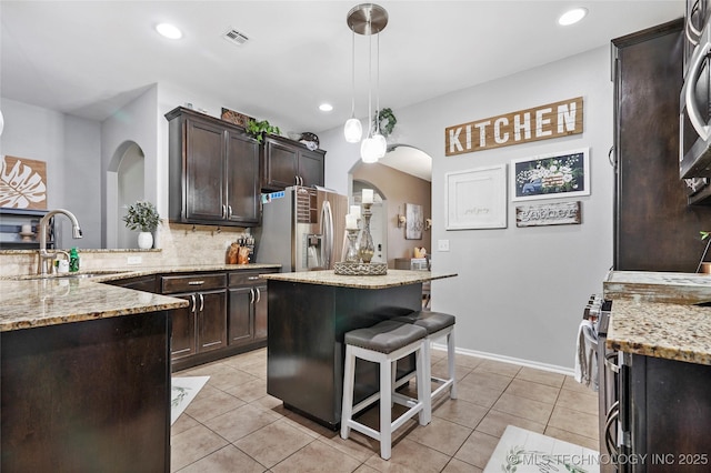 kitchen with appliances with stainless steel finishes, decorative light fixtures, tasteful backsplash, light stone countertops, and dark brown cabinets