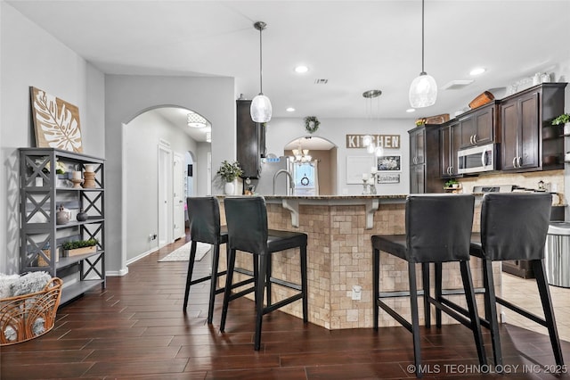 kitchen with pendant lighting, dark brown cabinetry, a kitchen breakfast bar, and appliances with stainless steel finishes