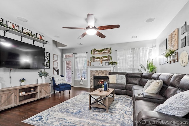 living room with ceiling fan, plenty of natural light, a stone fireplace, and dark hardwood / wood-style flooring