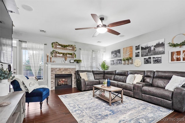 living room featuring ceiling fan, a stone fireplace, and dark hardwood / wood-style flooring