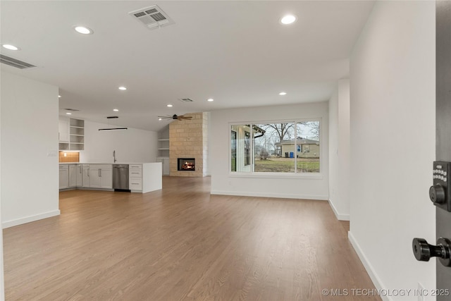 unfurnished living room with sink, light hardwood / wood-style flooring, ceiling fan, a large fireplace, and vaulted ceiling