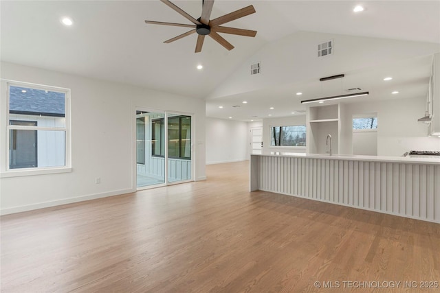 unfurnished living room with high vaulted ceiling, sink, ceiling fan, and light hardwood / wood-style flooring