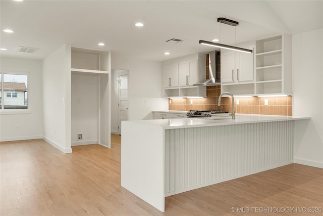 kitchen featuring wall chimney exhaust hood, white cabinetry, hanging light fixtures, light wood-type flooring, and kitchen peninsula