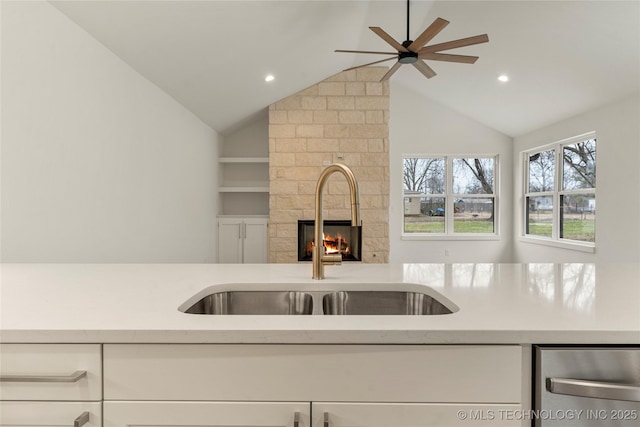 kitchen featuring lofted ceiling, sink, white cabinetry, ceiling fan, and a fireplace