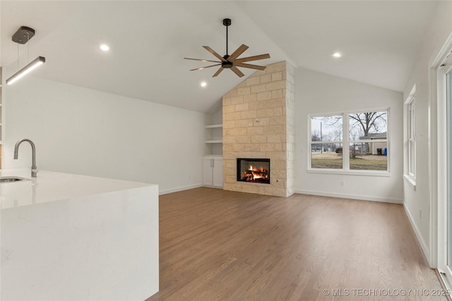 unfurnished living room with built in features, a fireplace, wood-type flooring, lofted ceiling, and sink