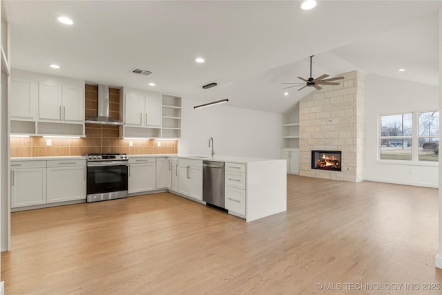 kitchen featuring wall chimney exhaust hood, white cabinetry, light hardwood / wood-style flooring, appliances with stainless steel finishes, and ceiling fan