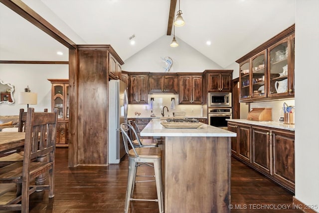 kitchen featuring dark wood-type flooring, appliances with stainless steel finishes, beam ceiling, dark brown cabinetry, and a kitchen island