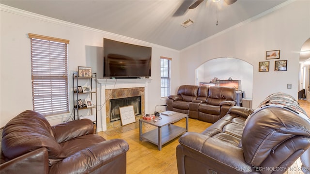 living room featuring ceiling fan, ornamental molding, a tiled fireplace, and light wood-type flooring