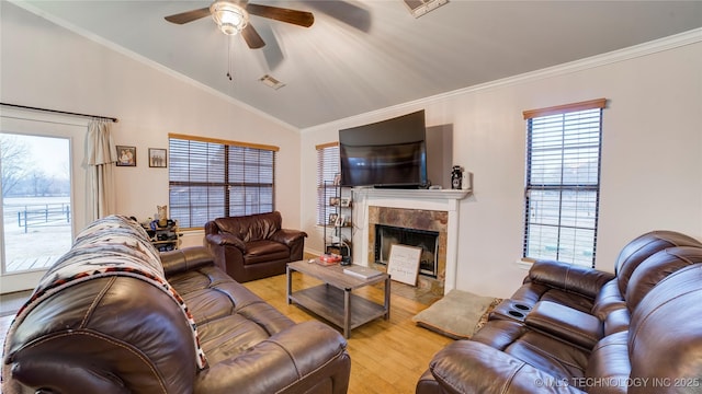 living room featuring crown molding, a tiled fireplace, vaulted ceiling, and light hardwood / wood-style flooring