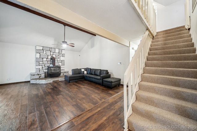 living room with lofted ceiling with beams, a wood stove, dark wood-type flooring, and ceiling fan