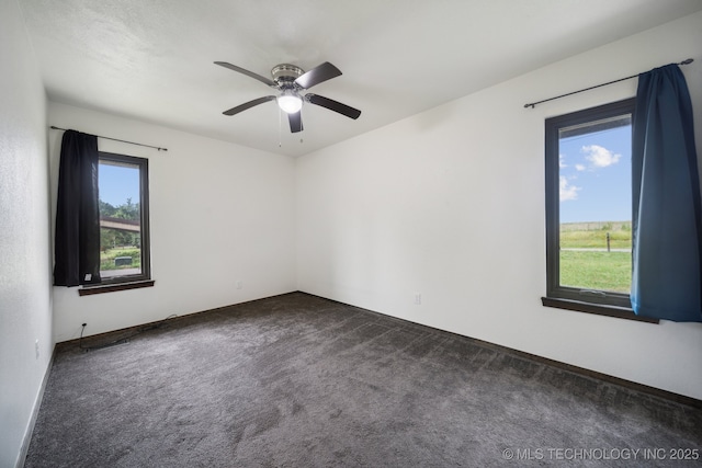 spare room featuring dark colored carpet, a healthy amount of sunlight, and ceiling fan