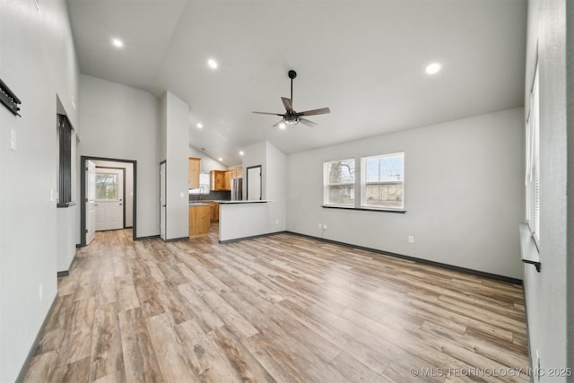 unfurnished living room with ceiling fan, high vaulted ceiling, sink, and light wood-type flooring