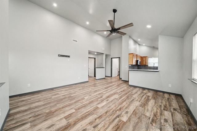 unfurnished living room featuring ceiling fan, light hardwood / wood-style flooring, and a towering ceiling