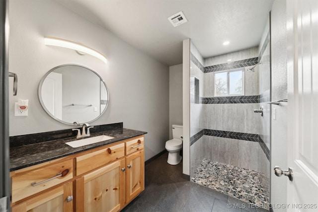 bathroom featuring tile patterned flooring, vanity, tiled shower, and toilet