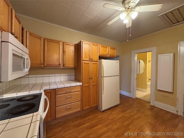 kitchen featuring tile countertops, ornamental molding, ceiling fan, white appliances, and light hardwood / wood-style flooring