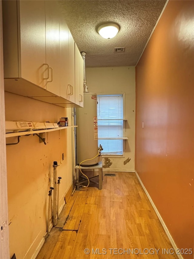 hall with light wood-type flooring, a textured ceiling, and gas water heater