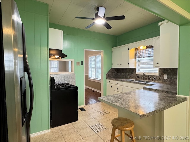 kitchen with sink, stainless steel fridge, stove, white cabinetry, and a kitchen breakfast bar