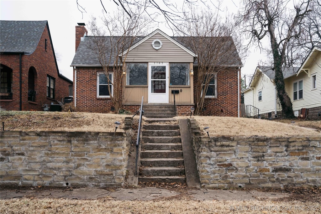 bungalow featuring entry steps, brick siding, and a chimney