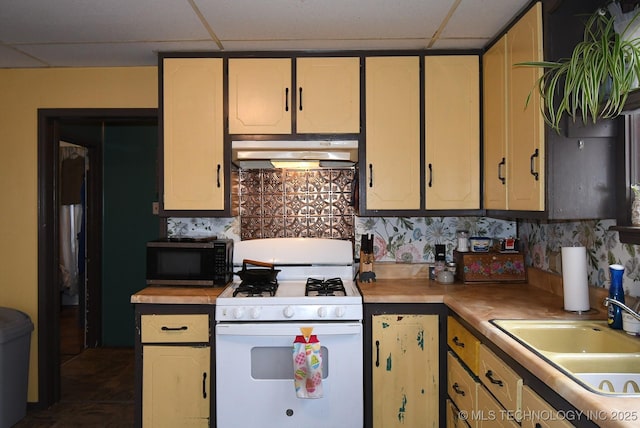 kitchen featuring a drop ceiling, sink, backsplash, and white gas stove