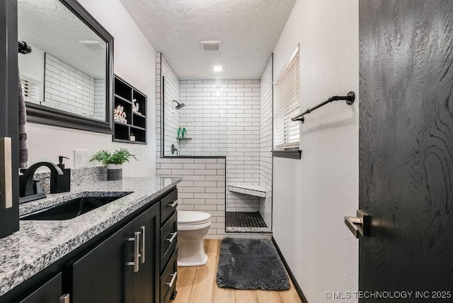 bathroom featuring vanity, hardwood / wood-style floors, a textured ceiling, and a tile shower