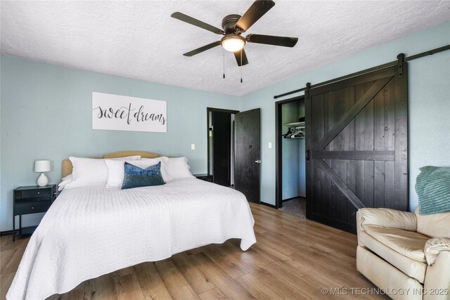 bedroom featuring wood-type flooring, a textured ceiling, a closet, ceiling fan, and a barn door