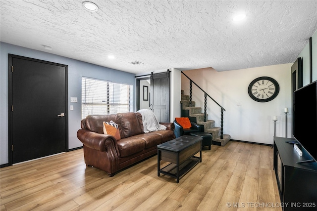 living room with a barn door, a textured ceiling, and light wood-type flooring