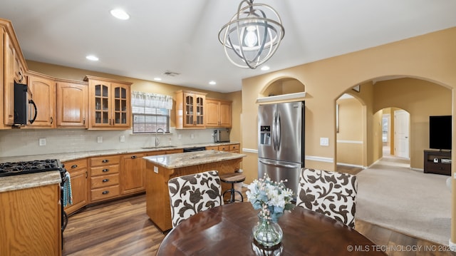 kitchen featuring appliances with stainless steel finishes, sink, hanging light fixtures, a center island, and light stone countertops