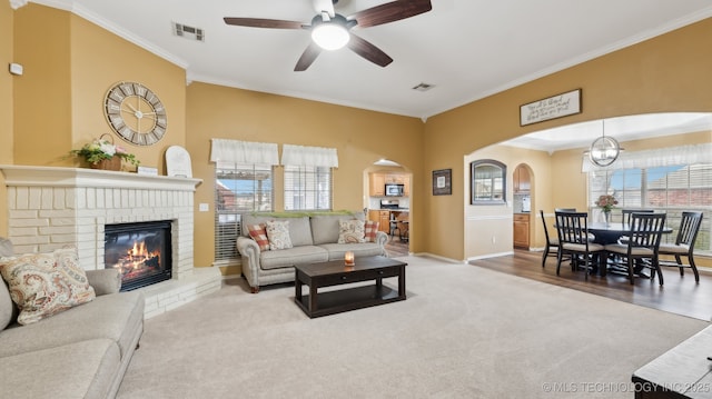 living room with ornamental molding, carpet, ceiling fan, and a brick fireplace