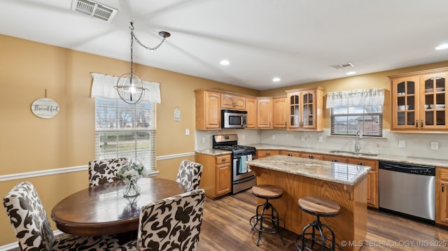 kitchen with a kitchen island, sink, dark hardwood / wood-style flooring, light stone counters, and stainless steel appliances