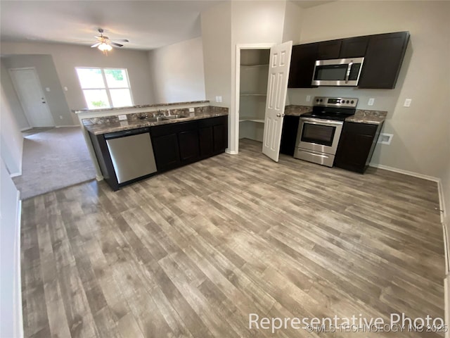 kitchen with appliances with stainless steel finishes, kitchen peninsula, light stone counters, and light hardwood / wood-style floors